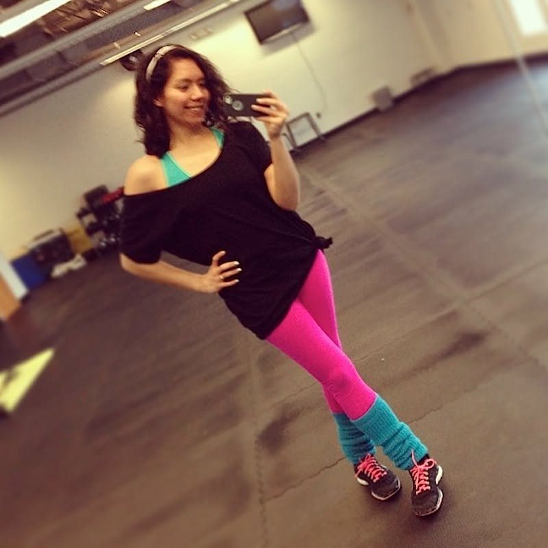 Woman in black oversized shirt and bright pink leggings posing for a selfie in a gym.