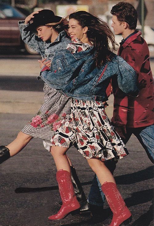 Two women in denim jackets and patterned skirts dancing while wearing red cowboy boots.