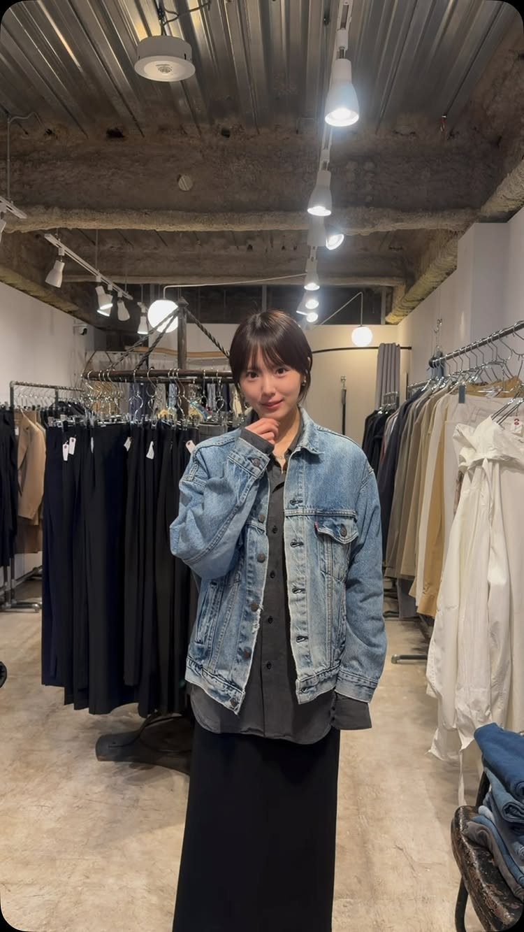 A woman posing in a clothing store wearing an oversized light blue denim jacket.