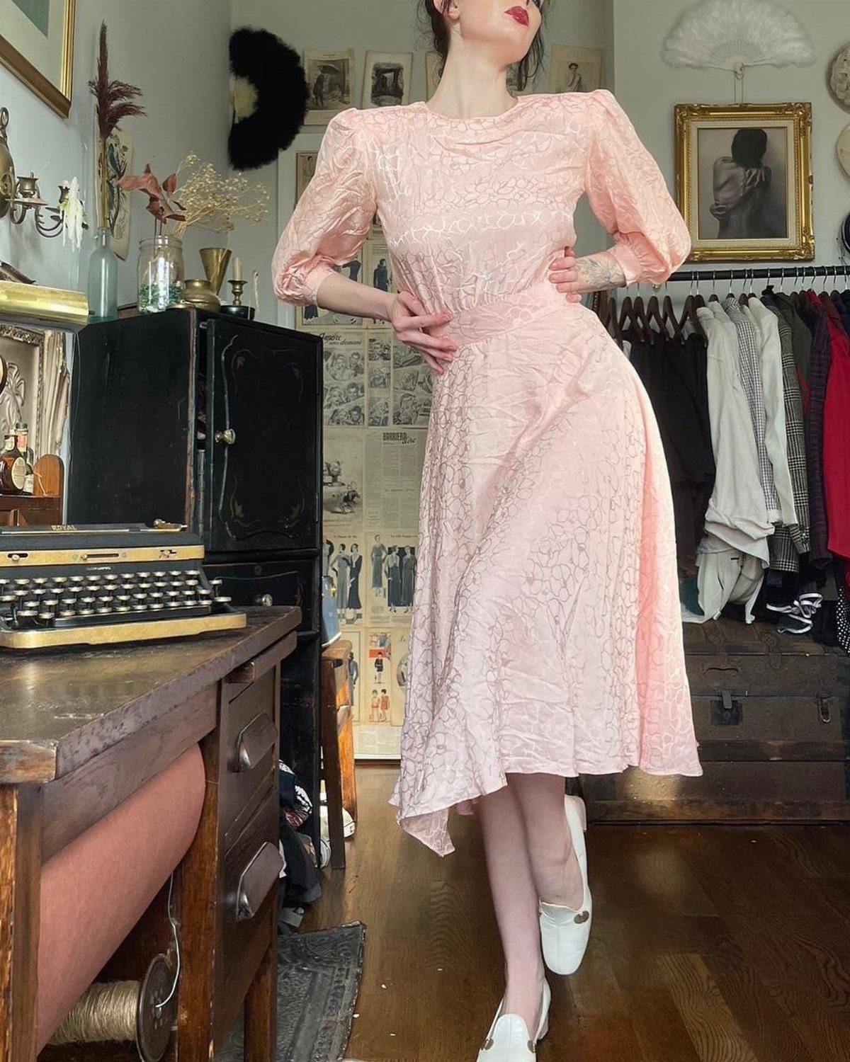 Woman posing in a light pink dress featuring distinct padded shoulders and long sleeves.