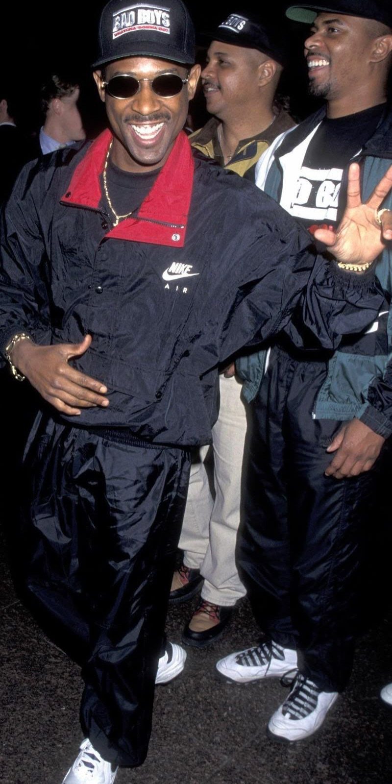 Man smiling in a black Nike windbreaker jacket and matching black track pants.