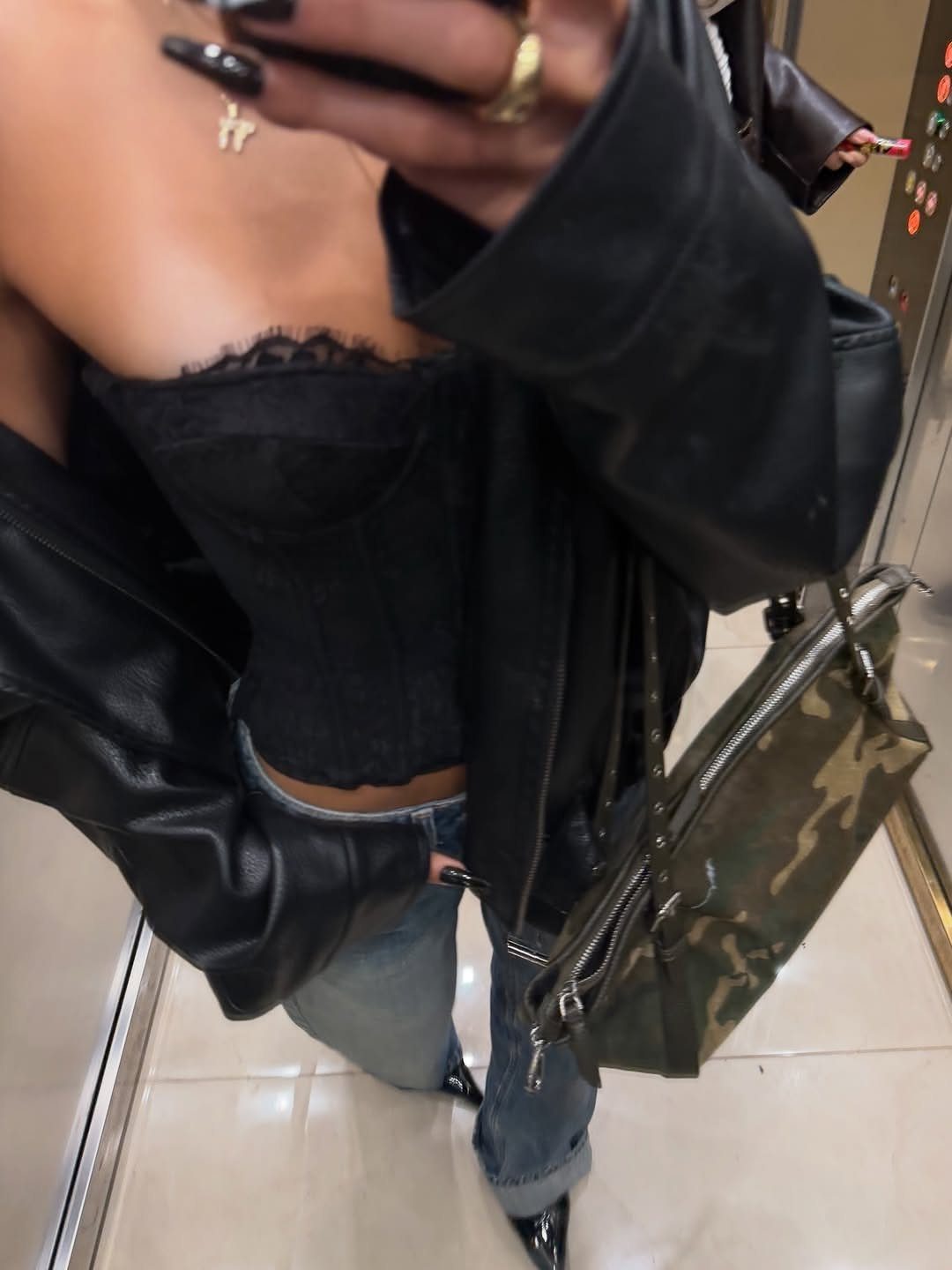 A person posing in a black lace corset, leather jacket, and blue jeans.