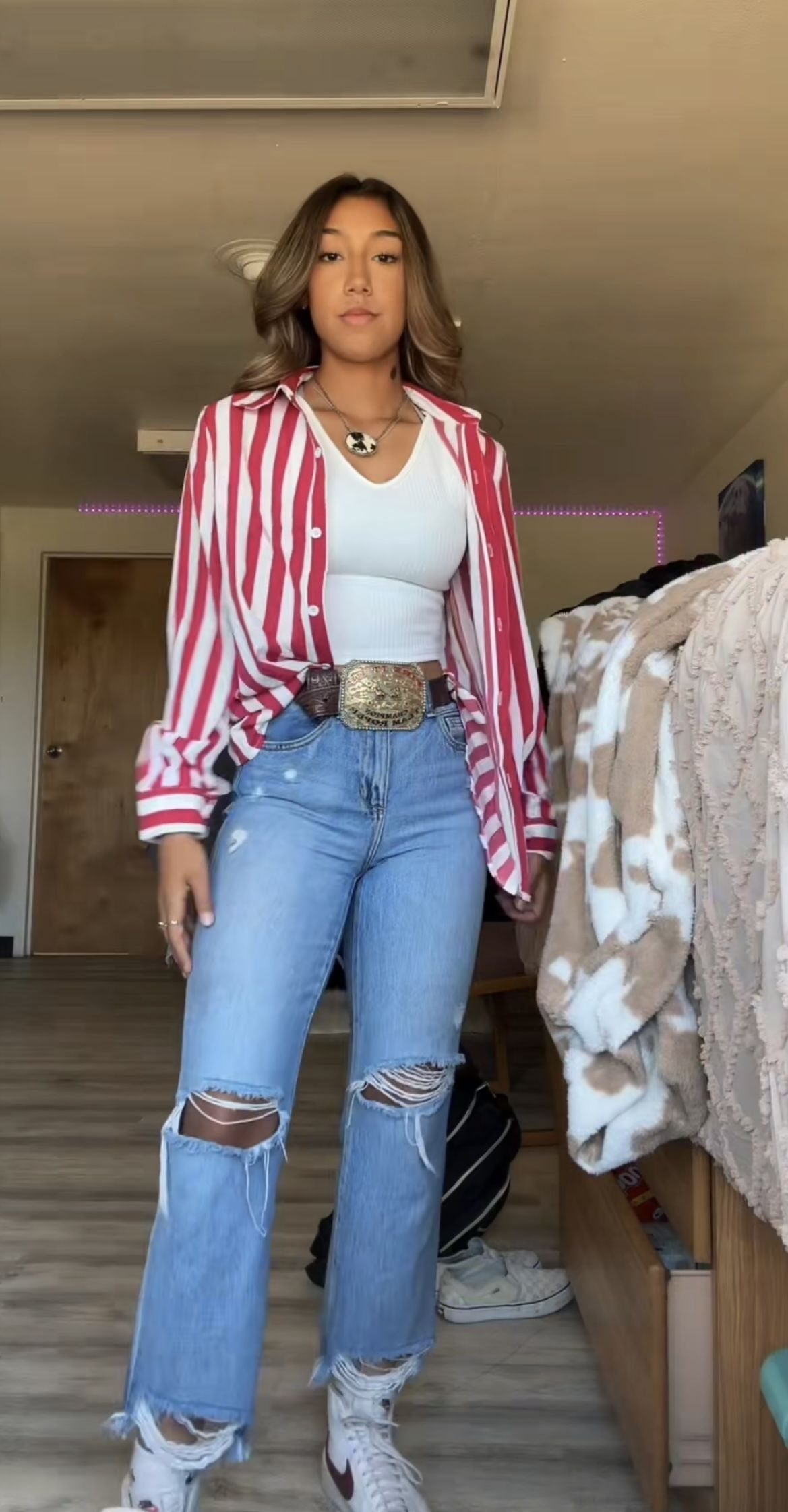 Woman wearing a red and white striped shirt with ripped bootcut jeans and a large belt buckle.