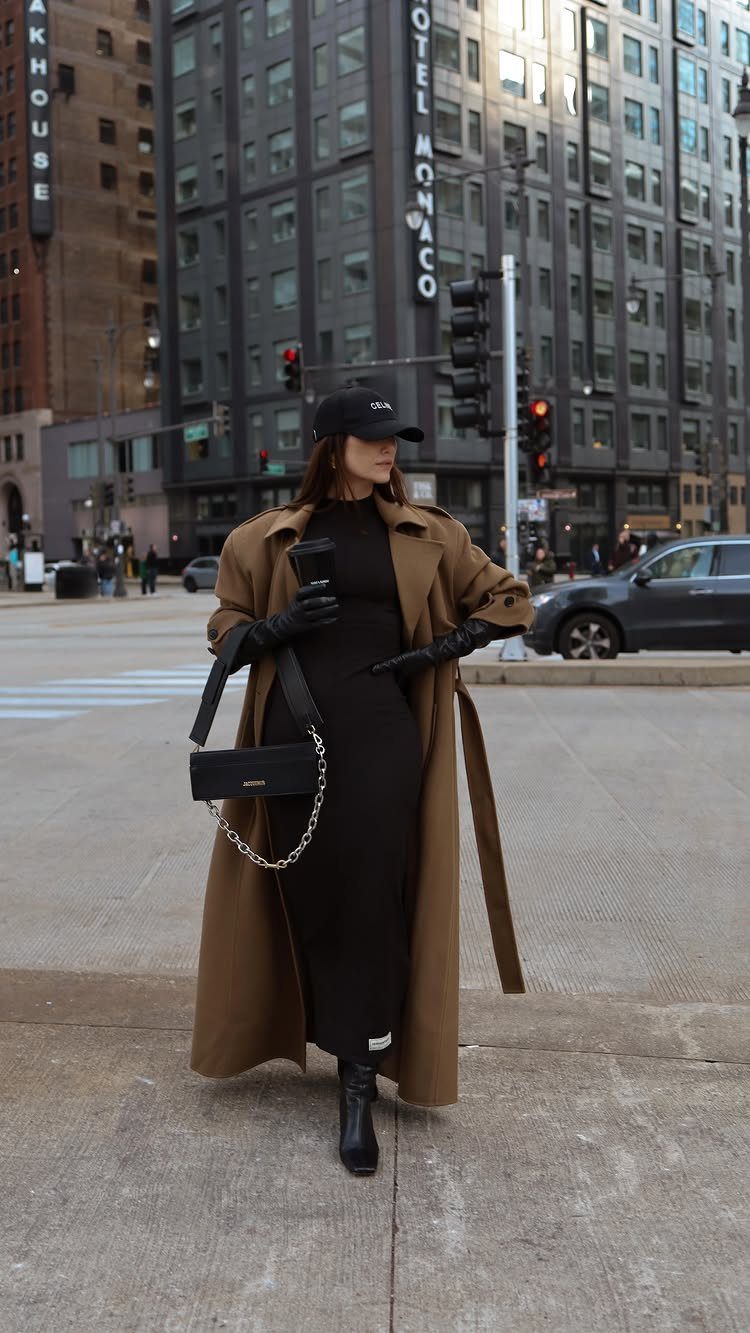 Woman in a black dress and tan trench coat walking on a city street.
