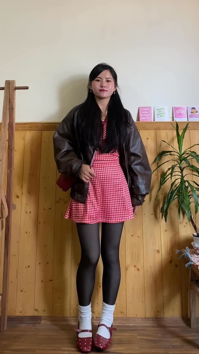 Woman wearing a red checkered mini dress, brown leather jacket, black tights, and red shoes.