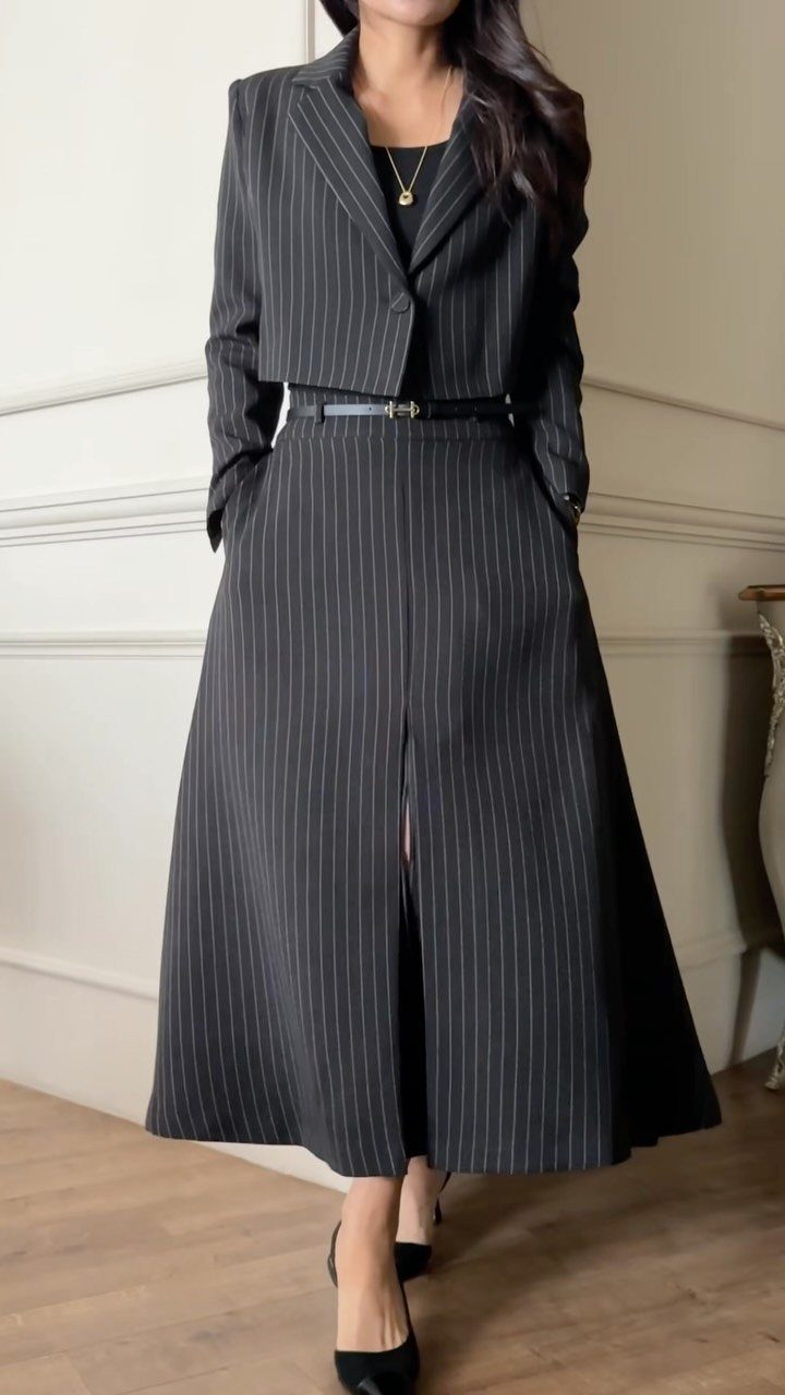 Woman wearing a black pinstriped cropped blazer and a matching midi skirt with a slit.