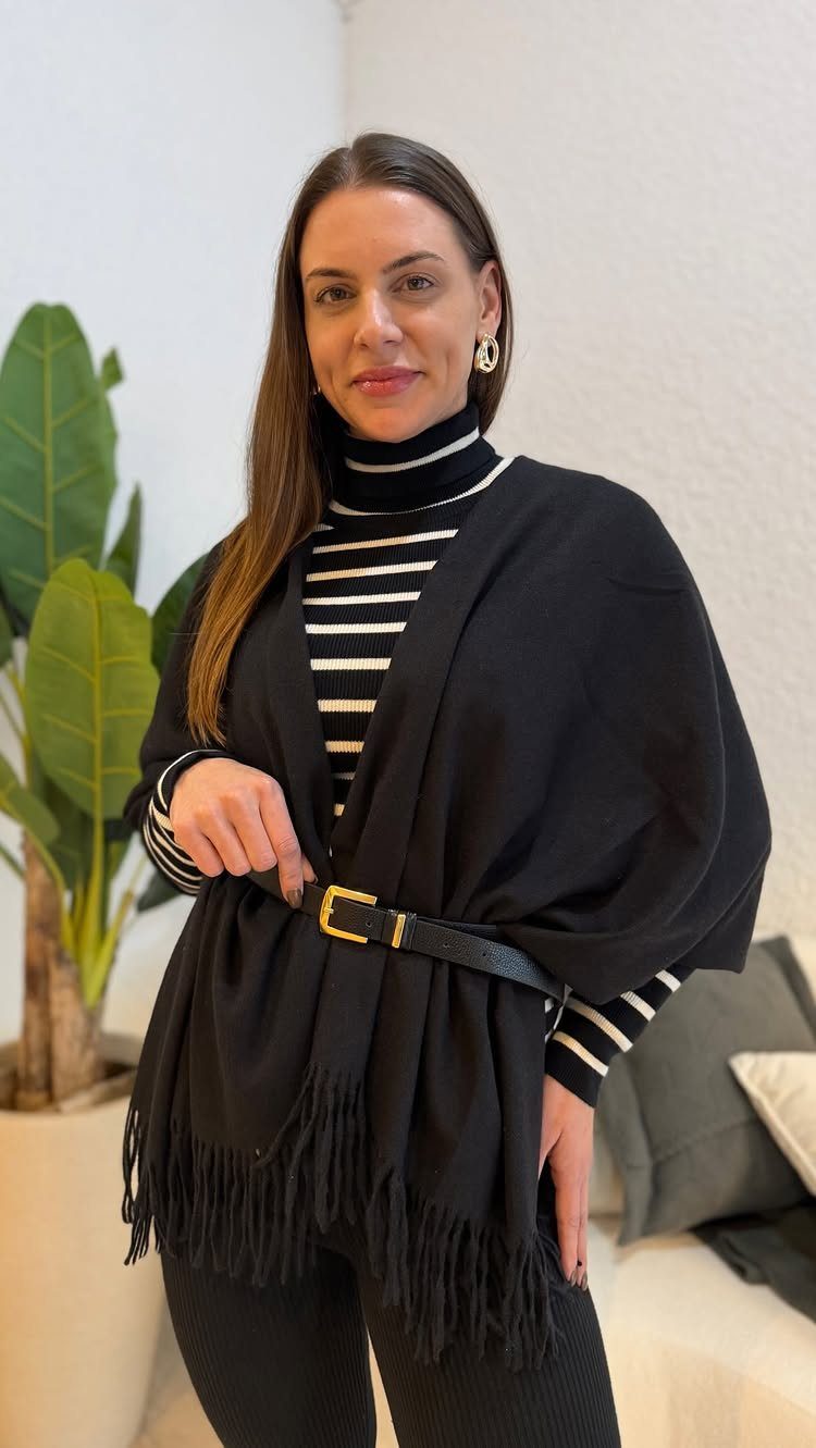 A woman wearing a striped turtleneck and a black fringed wrap cinched with a belt.