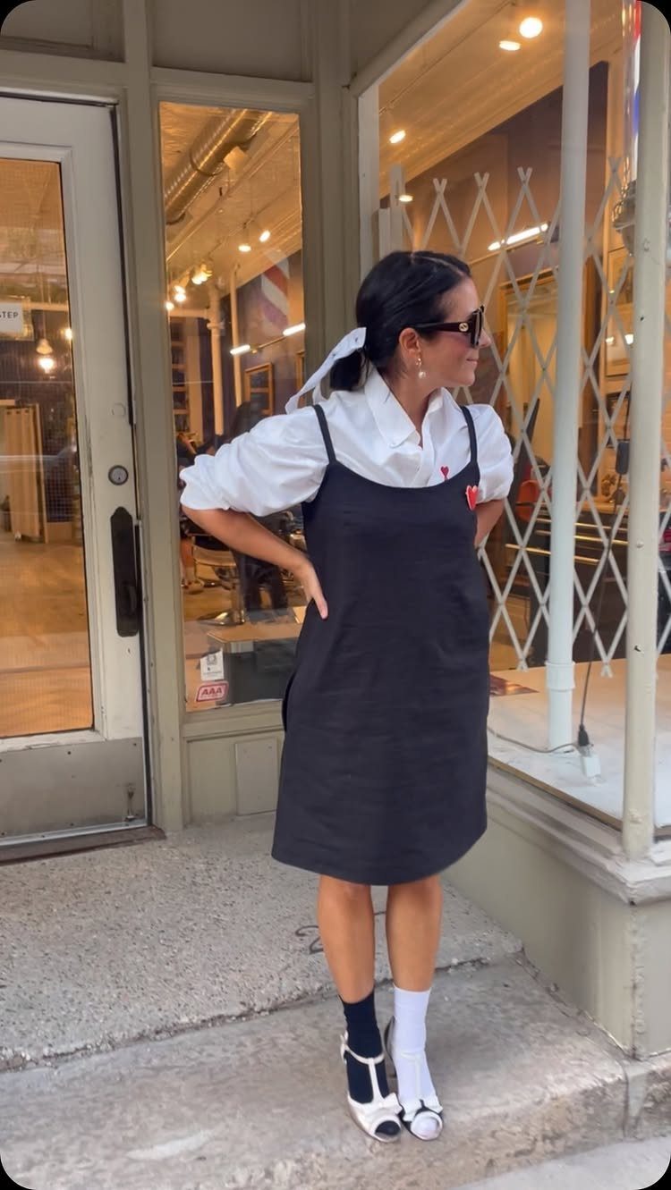 Woman wearing a white shirt layered under a black dress and patterned socks.