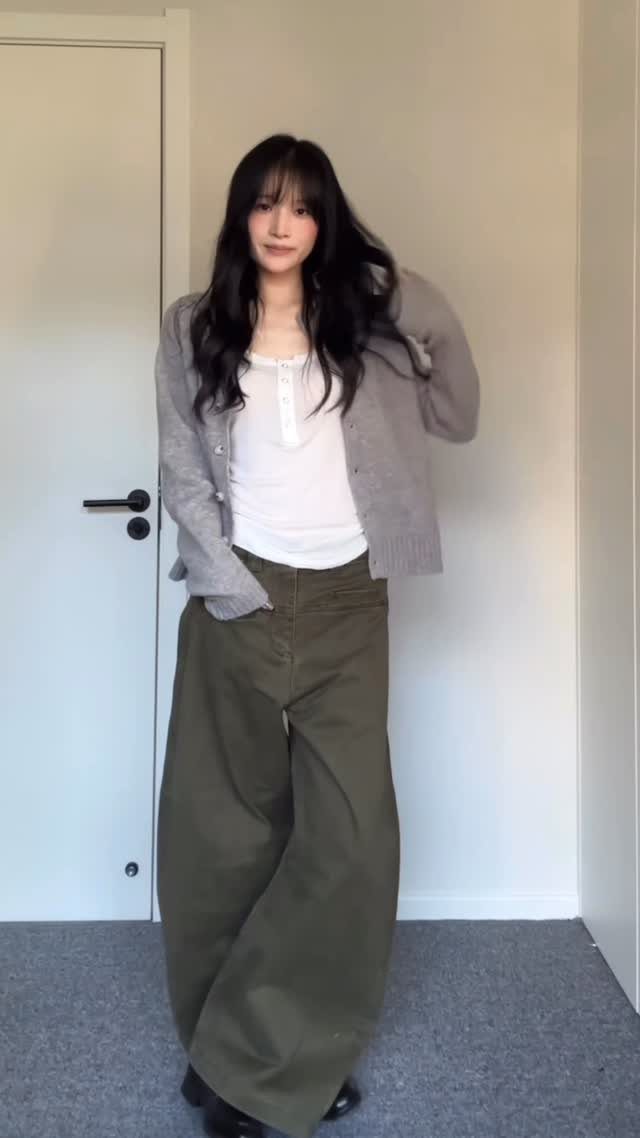 Woman wearing a white tank top, grey cardigan, and olive green wide-leg trousers.