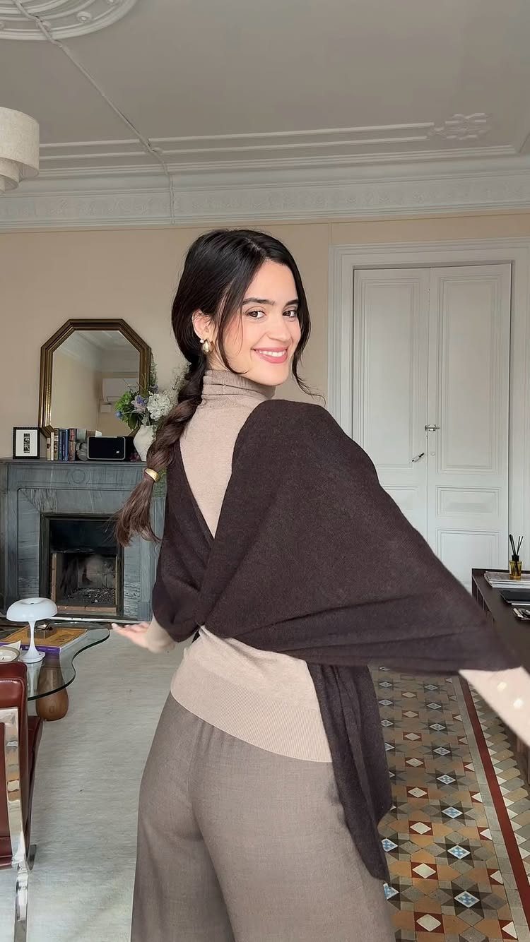 Smiling woman wearing a beige turtleneck with a dark brown knit wrap draped over her shoulders.