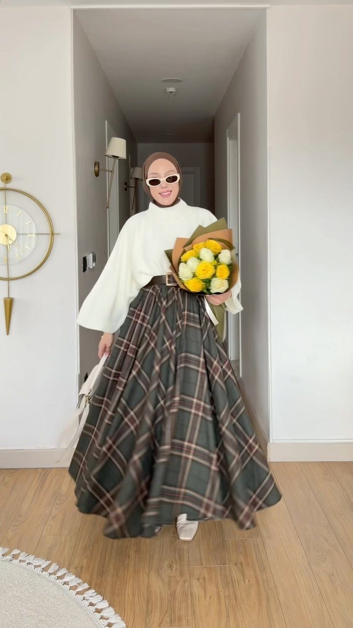 Woman in a white long-sleeve blouse and green plaid skirt holding yellow roses.