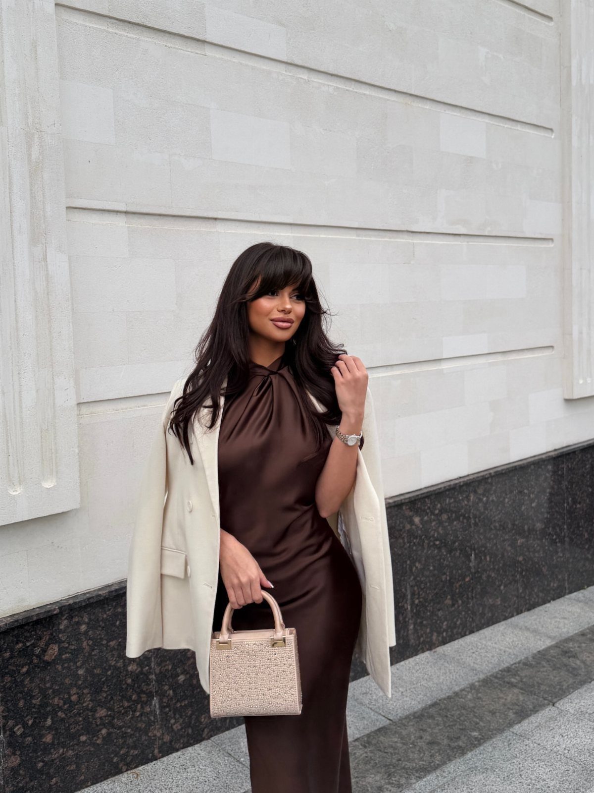Woman in brown satin dress with a cream blazer draped over her shoulders.