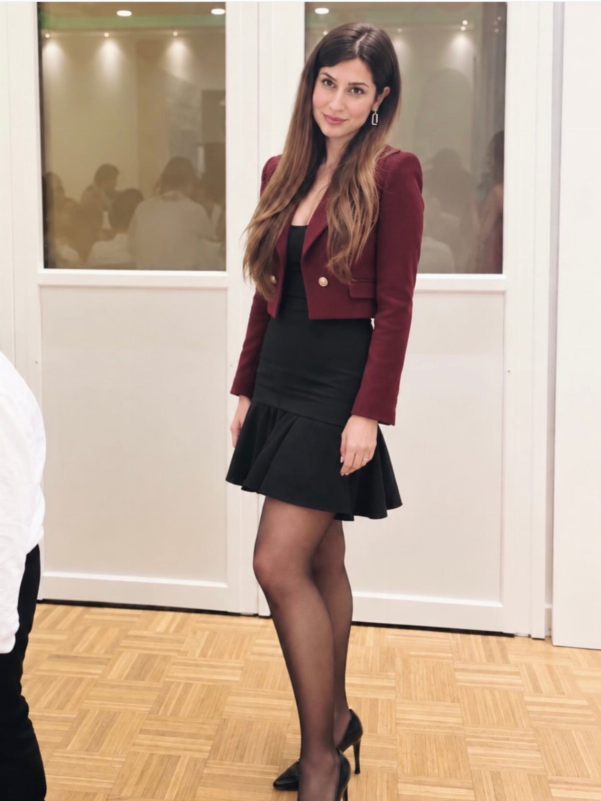 Woman wearing a black dress with a cropped burgundy blazer and black tights.