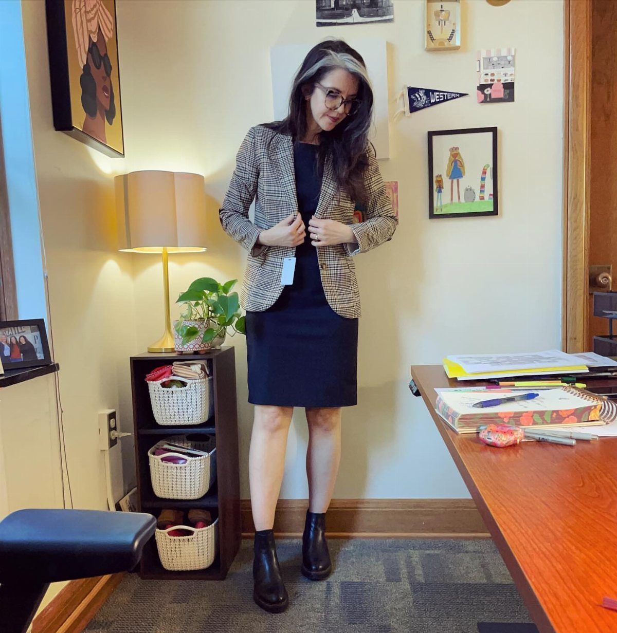 Woman wearing a black dress, patterned blazer, and black ankle boots in a room.