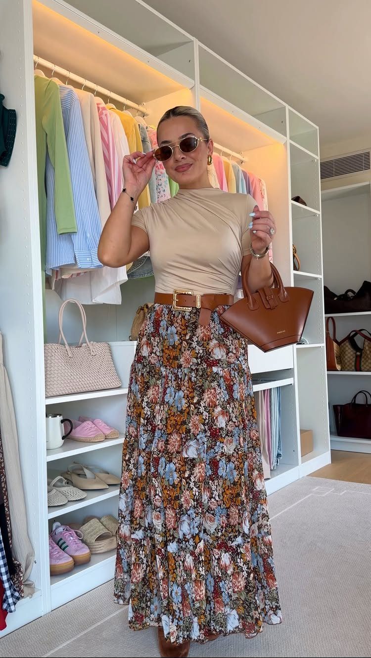 Woman posing in a tan top, brown belt, and long floral maxi skirt.