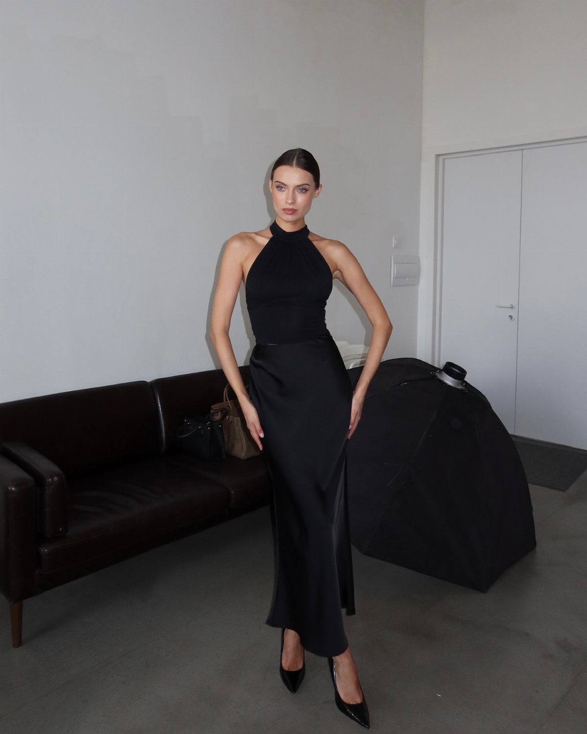 Woman posing in a black halter top and a long black maxi skirt with heels.
