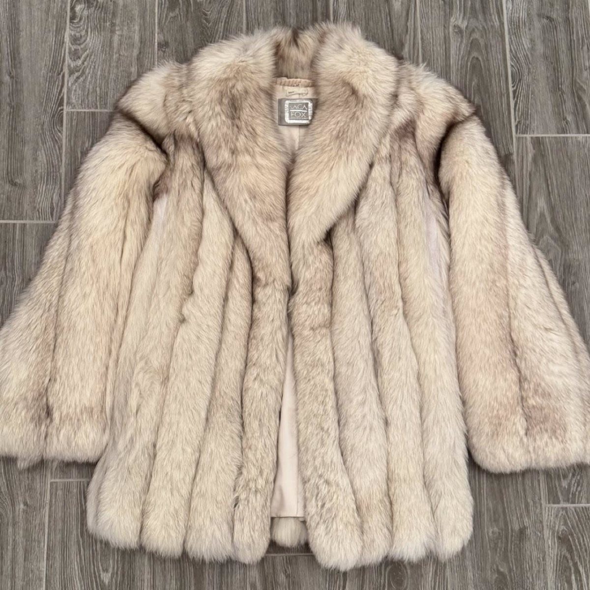 A thick, cream-colored arctic fox fur coat lying flat on a grey wooden floor.