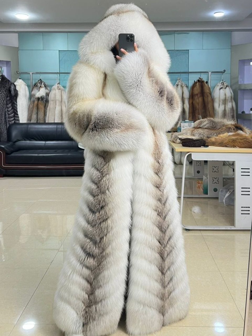 A person wearing a long, voluminous white and grey arctic fox fur coat in a showroom.
